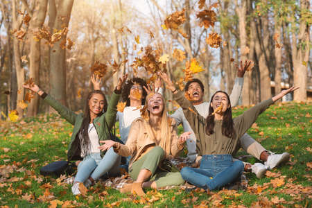 Young international friends playing with autumn leaves in public park, taking autumn photos togetherの写真素材