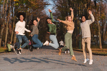 Joyful group of international teen friends jumping in the air, having fun in parkの写真素材