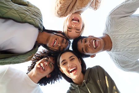 Smiling multiracial group of young friends forming circle of heads and looking at camera, friendship...