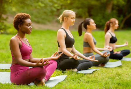 Sporty millennial girls of different races doing yoga meditation at park, empty spaceの写真素材