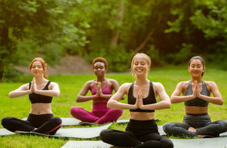 Happy multiethnic women meditating during their morning yoga practice at park, copy spaceの写真素材