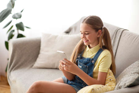Amazing Application. Casual glad teenage kid with ponytails using smart phone, typing and sending messageの写真素材