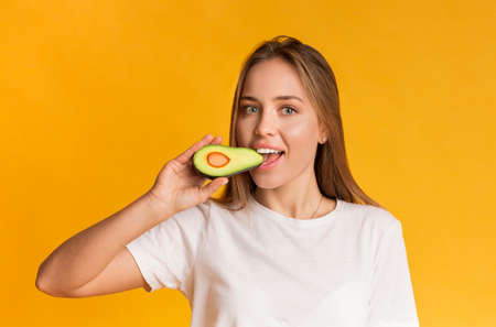 Healthy Fats. Beautiful Girl Eating Avocado, Biting Fruit Half, Smiling At Camera While Posing Over Yellow Background In Studio, Free Spaceの写真素材