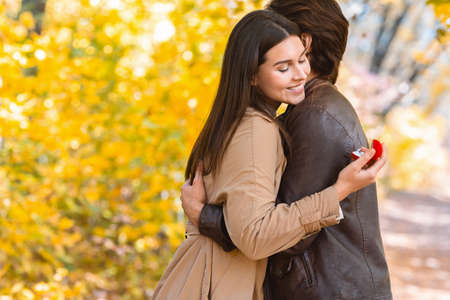 Marriage proposal at autumn forest. Happy woman looking at proposal ring while hugging her boyfriend, copy spaceの写真素材