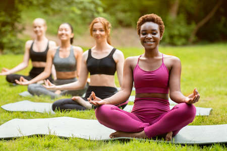 Beautiful black girl with her friends meditating on group yoga class at park, copy spaceの写真素材