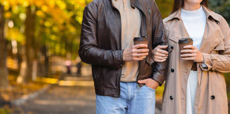 Cropped of man and woman drinking coffee while walking by autumn forest, panorama with free spaceの写真素材