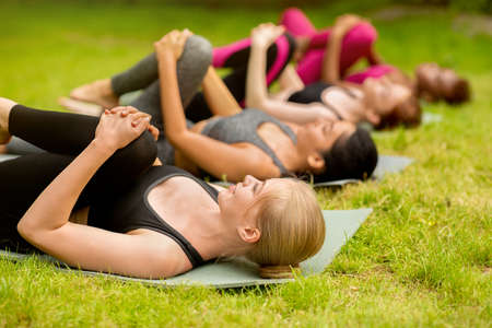 Multinational women doing flexibility exercises during yoga class at park. Blank space