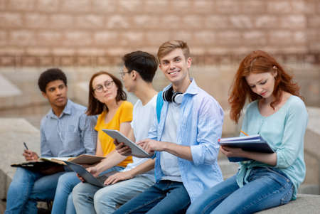 Happy Student Guy Smiling To Camera Sitting Among Group Of Coursemates Learning After Classes...
