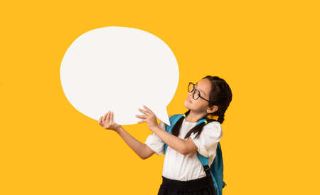 Japanese Schoolgirl Holding Blank Speech Bubble Standing Over Yellow Background. Studio Shot, Mockup