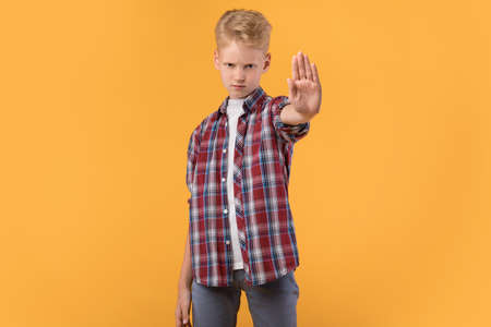 Domestic Violence And Child Abuse. Serious boy making stop hand gesture to camera, pastel orange...