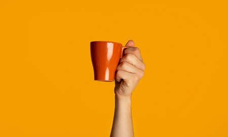 Young guy holding mug with yummy hot drink on orange background, closeup view. Panoramaの写真素材