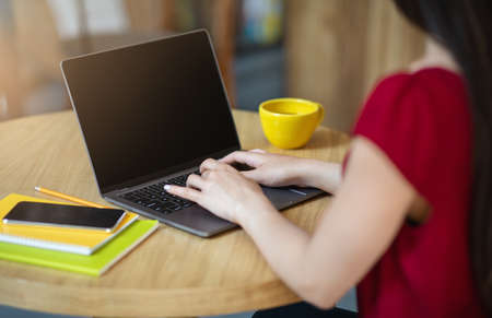 Unrecognizable woman typing on laptop with black blank screen in cafe, mockup image with copy space