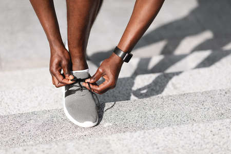Unrecognizable Black Athlete Tying Laces On Sport Shoes Before Running Outdoors, Cropped Image, Closeup With Free Spaceの写真素材