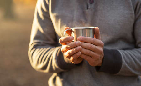 Male hands holding warm cup of tea or coffee, forest background, closeup