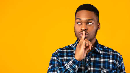 Its Secret. Black Guy Putting Finger On Lips Making Hush Sign Posing Over Yellow Studio Background....