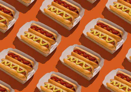 Two hotdogs with mustard and ketchup in carton packing over orange background, seamless pattern, creative geometrical design, top viewの写真素材