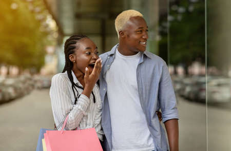 Sale, consumerism and people. Surprised african american couple with bags looking at showcase of boutique outdoorsの写真素材