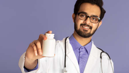 Smiling Indian doctor showing jar of pills on violet background, mockup for design. Selective focus. Panoramaの写真素材