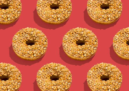 Many delicious donuts with chocolate caramel glaze and nuts sprinkles over pink background, creative design, repeat pattern, top viewの写真素材