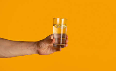 Young man holding glass of clear drinking water on orange background, closeup. Panoramaの写真素材