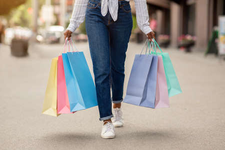 Shopping with bonuses and gifts. African american woman with many colored bags walks down the street from storeの写真素材