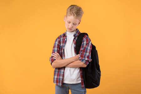 Feeling Offended. Portrait of upset boy standing with folded arms looking down isolated on pastel orange studio wallの写真素材