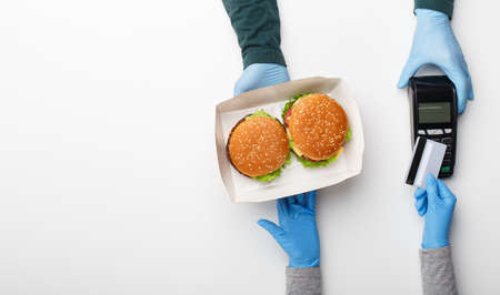 Courier delivered box with hamburger and cheeseburger to home. Customer in rubber gloves pay by credit card at contactless terminal isolated on white background, top view, panorama, free space, panoramaの写真素材