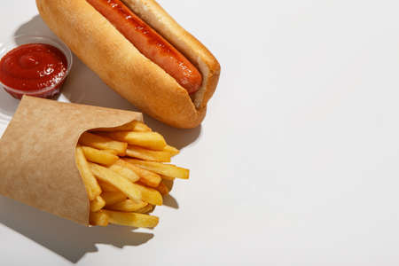 Fast food isolated on white background. French fries in eco pack, hot dog, and ketchup in container, flat lay, close up, free spaceの写真素材