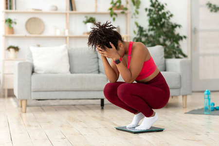 Desperate Black Girl Crying Standing On Weight-Scales Slimming, Not Losing Weight On A Diet At Home. Copy Spaceの写真素材