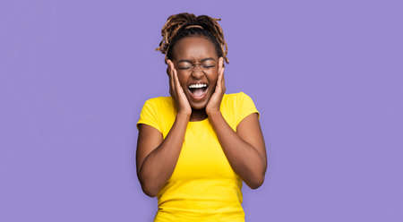 Emotional african girl with closed eyes touching her face and screaming, expressing happiness,...
