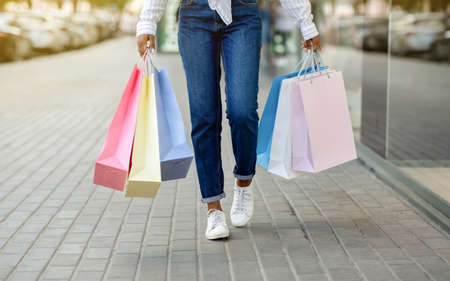 Shopaholic on walk. African american girl with many colored bags walks from store, outdoors,...