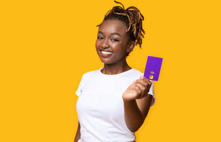 Happy african girl recommending credit card, yellow studio background, copy space