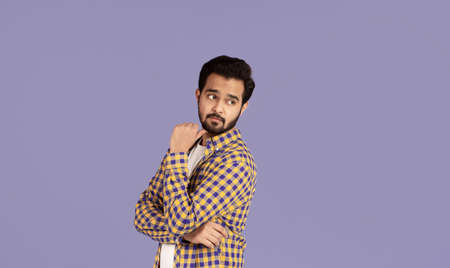 Thoughtful Indian guy looking over his shoulder at empty space, lilac background. Panorama