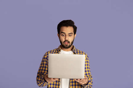 Shocked Indian guy staring at laptop screen with open mouth on lilac backgroundの写真素材