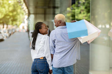 Happy african american couple with many colored bags walking from store after shopping, outdoors,...