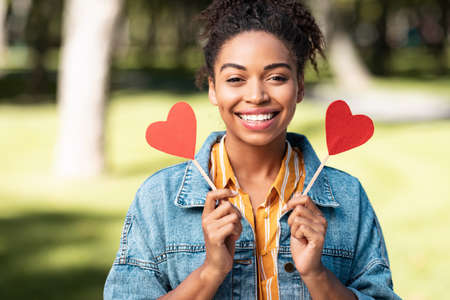 Love. Happy African Girl Holding Paper Hearts Smiling To Camera Standing Outside In Parkの写真素材