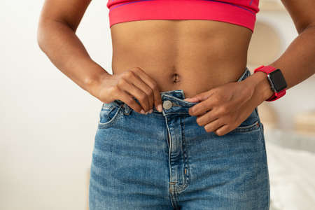 Black Girl After Weight Loss Buttoning Skinny Jeans Standing Indoors. Perfect Size Concept. Croppedの写真素材