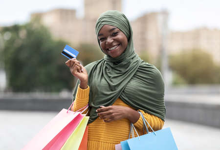 Smiling Black Musim Woman Posing With Colorful Shopping Bags And Credit Card Outdoors, Enjoying Seasonal Sales And Easy Payments, Received Cashback Bonus Discount, Looking At Camera, Copy Spaceの写真素材