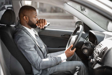 Pensive african american young businessman driving expensive car, going to office in the morning....