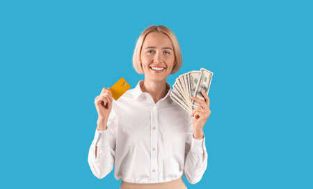 Portrait of happy businesswoman holding money and credit card over blue studio background, panorama....