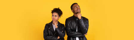 Thoughtful African American Couple Thinking Posing Standing Back-To-Back On Yellow Studio Background, Wearing Black Leather Jackets. Female And Male Thoughts Concept. Panorama With Copy Spaceの写真素材