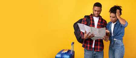 African Tourists Couple Having Problem Planning Vacation Holding Map Choosing Destination Standing Over Yellow Background In Studio. Travel Navigation Problems Concept. Panorama With Copy Spaceの写真素材