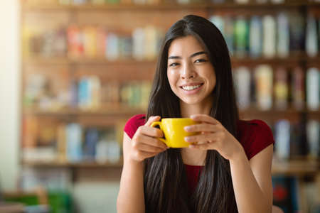 Tea Time. Portrait Of Smiling Asian Woman With Mug Of Hot Drink In Cafe, Looking At Camera, Copy Spaceの写真素材