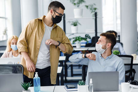 Safe hello at work during COVID-19 epidemic and social distance. Young men in protective masks greet...