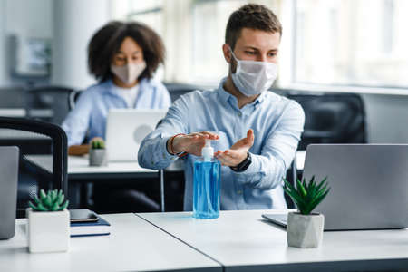 Protection at coronavirus pandemic in office. Young man in protective mask works at laptop and...