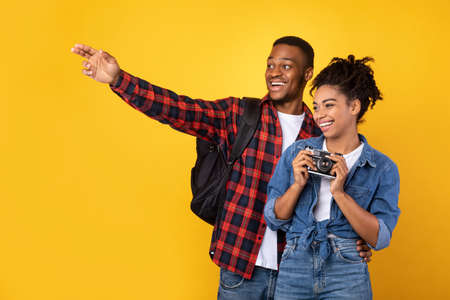 Cheerful African Travelers Couple With Photo Camera Taking Pictures Traveling Together On Vacation Standing On Yellow Studio Background. Tourism Concept, Tourists On Sightseeing Tourの写真素材