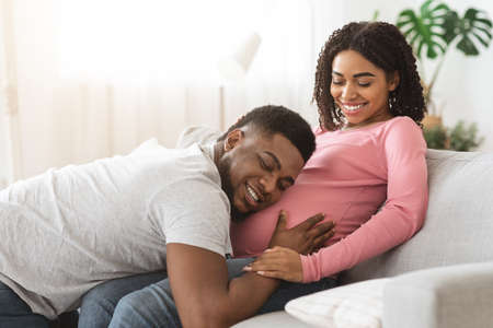 Happy black man listening to his pregnant wife big belly. Fatherhood concept. Loving african...