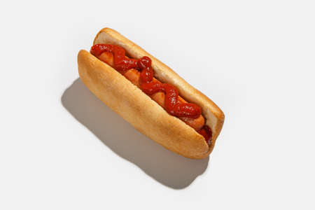 Delicious fast and junk food for snack. Hot dog with bun, grilled sausage and ketchup with shadow in menu for client order at home isolated on white background, cut out, top view, free spaceの写真素材
