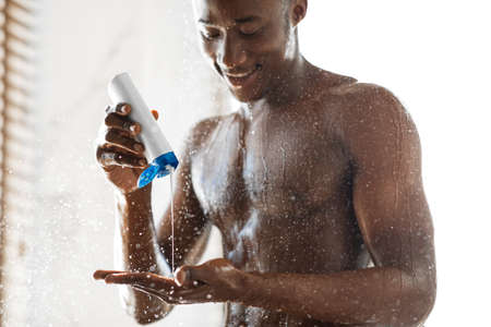 Black Guy Pouring Shampoo On Hand Washing Hair Taking Shower Standing Under Water In Bathroom At Home.の写真素材