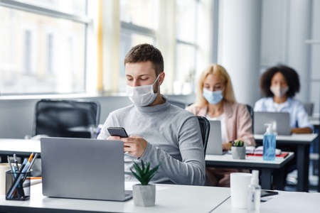 Modern technology for work during quarantine covid-19. Young man manager in protective mask typing...